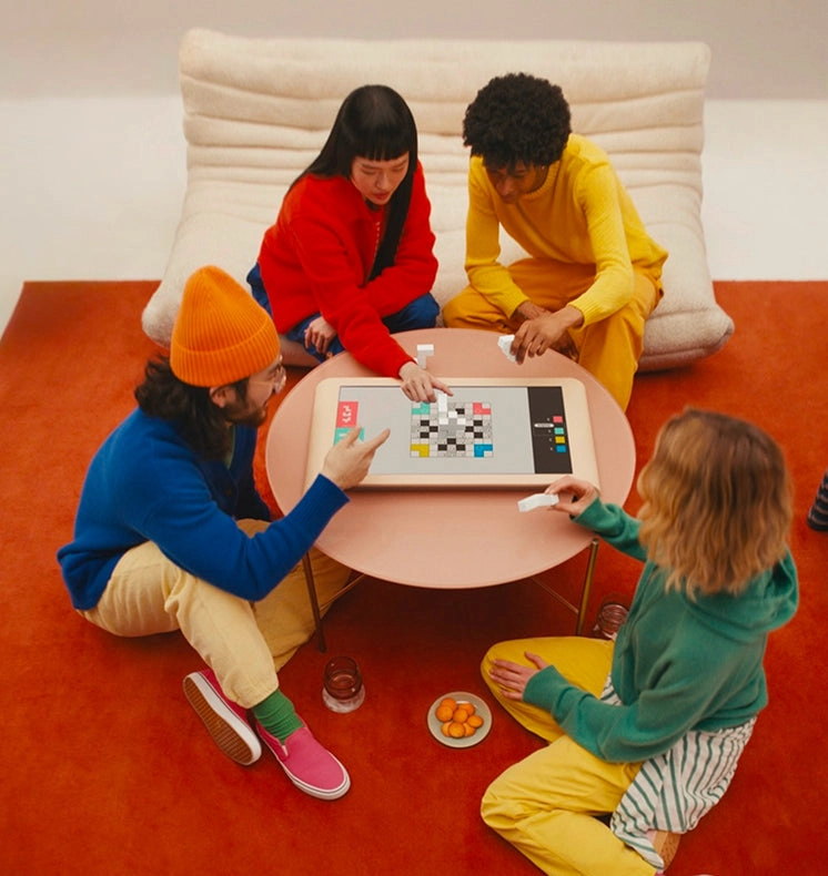 Four friends gathered around a Board tabletop game console playing together in a living room.